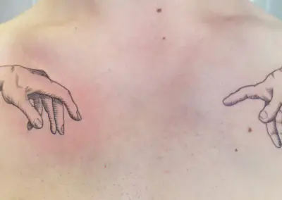 Tatouage fine line des mains de la Création d'Adam sur le haut du dos