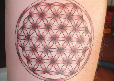 Tatouage fleur de vie géométrique rehaussé de rouge sur la cuisse