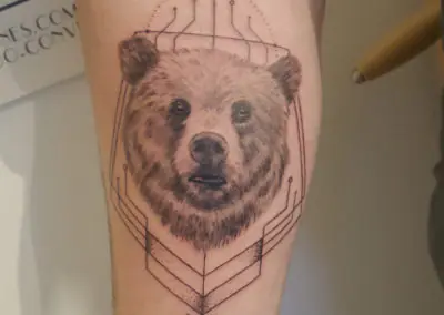 Tatouage d'ours réaliste sur fond géométrique, avant-bras